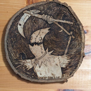 May include: A woodburned design on a wood slice featuring a scarecrow-like figure with a scythe and the text "Stay Up Stay Low" and "XXVII".