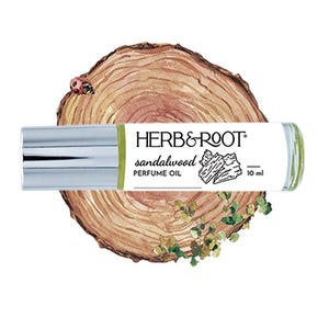 May include: A sandalwood perfume oil roll-on bottle with a silver cap, labeled "HERB & ROOT." The bottle is set against a backdrop of a wood slice with a ladybug and greenery. The bottle contains 10 ml of perfume.