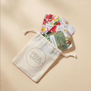 May include: A beige drawstring pouch with the text Herb & Root printed in a circle on the front. Inside the pouch are several rectangular cards featuring colorful floral and botanical patterns, with labels including midnight, fuji, and hummingbird.