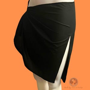 May include: A black wrap-style pareo skirt featuring a high side slit and a smooth, solid-colored fabric construction. The garment is displayed on a mannequin and includes the text "SPLIT PAREO" in bold blue letters and a circular logo with text.