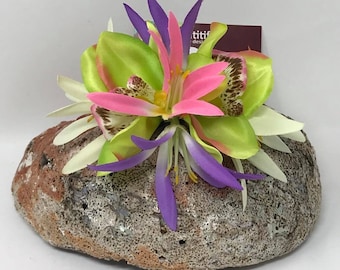 Peut inclure: Un petit rocher texturé gris avec un groupe de fleurs artificielles sur le dessus. Les fleurs sont roses, vertes et violettes.