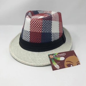 May include: A white and blue checkered fedora hat with a black band. The hat is made of woven straw and has a wide brim. The hat is sitting on a white surface.