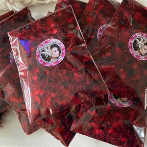 May include: Multiple clear plastic pouches filled with small, dark red, petal-like pieces. Each pouch features a circular sticker with a portrait of a person wearing a floral headpiece and the text Dare O'Latifa printed in a decorative font.