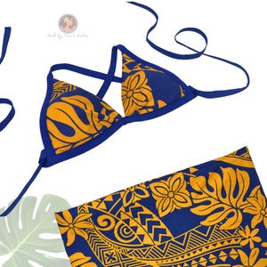 May include: A blue and yellow bikini top and matching sarong. The bikini top has a triangle design with yellow floral patterns and blue trim. The sarong features a similar pattern. The text "Made By Tina O'Paddlife" is visible in the image.