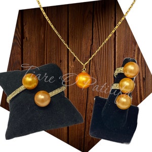 May include: A set of golden jewelry featuring a necklace with a large golden pearl pendant, a bracelet with two golden pearls, and a ring with three golden pearls.