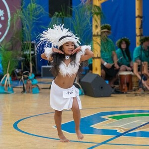 May include: A young girl in a white costume with feathers and a white skirt dances on a wooden floor. She is wearing a white flower necklace and has a number 46 on her skirt.