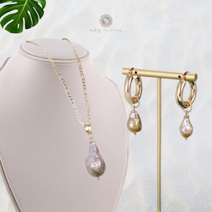May include: A gold chain necklace with a large, pearlescent, teardrop-shaped pendant. Matching gold hoop earrings with a similar pearlescent teardrop pendant dangle from each hoop.