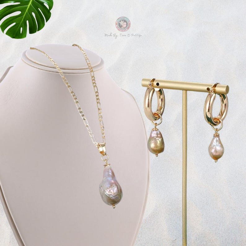 May include: A gold chain necklace with a large, pearlescent, teardrop-shaped pendant. Matching gold hoop earrings with a similar pearlescent teardrop pendant dangle from each hoop.