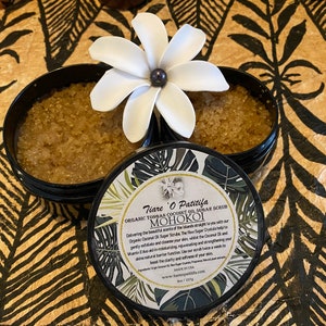K&ouml;nnte beinhalten: Ein schwarzer Topf mit einem wei&szlig;en Deckel, der ein braunes Zuckerschrub enth&auml;lt. Der Topf hat ein Etikett mit dem Text "Tiare O Patitifa Organic Tongan Coconut Oil Sugar Scrub MOHOKOI Delivering the beautiful scents of the Islands straight to you with our Organic Coconut Oil and Sugar Scrub. The Raw Sugar Crystals help to gently exfoliate and cleanse your skin, whilst the Coconut Oil and Vitamin E work in barrier function, rejuvenating and strengthening your skin's natural moisturising factors.  Our scrub helps to provide a warm, exotic add to the clarity and softness of your skin.  Made with the best of Tongan and Hawaiian natural plant ingredients.  Made in the USA. www.tiareopatitifa.com Net Wt 227g"
