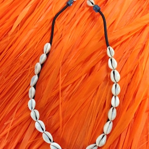 May include: A white shell necklace with a black cord. The necklace is on a bright orange background.