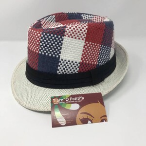 May include: A white and red checkered fedora hat with a black band. The hat is made of woven straw and has a wide brim. The hat is sitting on a white surface. The hat has a label that says "Tiare 'O Patitifa Polynesian costume design".