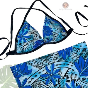 May include: A blue and white floral print bikini top and matching sarong. The bikini top has black trim and ties. The sarong features a similar floral pattern with blue flowers and leaf designs.