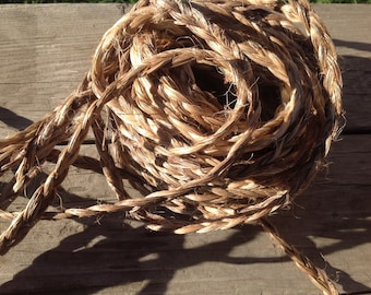 May include: A close-up of a coil of natural fiber rope. The rope is a light brown color and has a rough texture. It is coiled on a wooden surface.