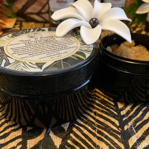 K&ouml;nnte beinhalten: Zwei schwarze Gl&auml;ser mit Deckeln. Das Glas links hat ein wei&szlig;es Etikett mit gr&uuml;nen Bl&auml;ttern und dem Text "Tiare O Paititi Organic Coconut Oil & Sugar Scrub  MOHOKOI Delivering the most decadent moisturizing, exfoliating and smoothing experience. Coconut oil, sugar, and essential oils are carefully blended to create a luxurious, conditioning scrub. Gently exfoliate, leaving your skin feeling soft and smooth.  Made in the USA.  Handcrafted with love.  Because real natural beauty shines through.  www.tiareopaititi.com  Net Wt. 3.5 oz"