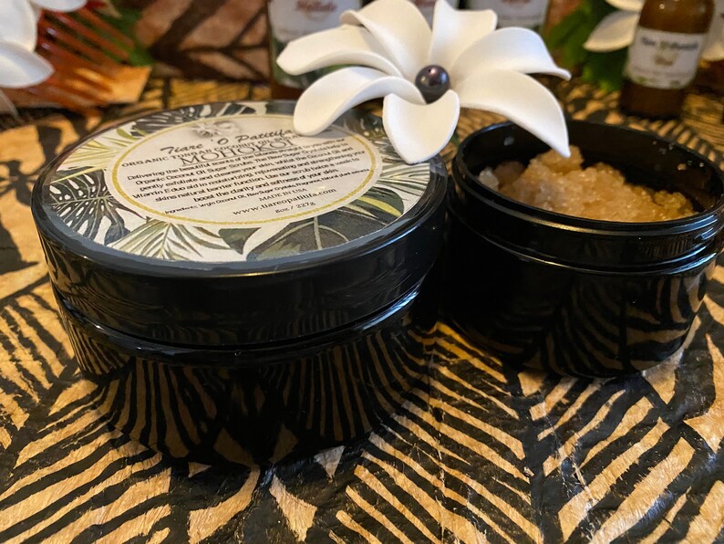 K&ouml;nnte beinhalten: Zwei schwarze Gl&auml;ser mit Deckeln. Das Glas links hat ein wei&szlig;es Etikett mit gr&uuml;nen Bl&auml;ttern und dem Text "Tiare O Paititi Organic Coconut Oil & Sugar Scrub  MOHOKOI Delivering the most decadent moisturizing, exfoliating and smoothing experience. Coconut oil, sugar, and essential oils are carefully blended to create a luxurious, conditioning scrub. Gently exfoliate, leaving your skin feeling soft and smooth.  Made in the USA.  Handcrafted with love.  Because real natural beauty shines through.  www.tiareopaititi.com  Net Wt. 3.5 oz"