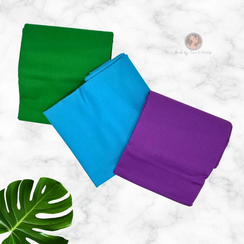 May include: Three folded pieces of solid-colored fabric in vibrant green, bright blue, and deep purple. Each piece is neatly stacked and arranged diagonally. A small circular logo with the text Made By Tiana O Pratile is visible in the corner.