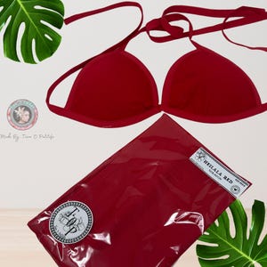 May include: Red bikini top with adjustable straps and a halter neck style. The top is made of a soft, stretchy fabric and has a triangle shape. The top is packaged in a clear plastic bag with a red label that says "Heilala Red Sun Rayon".