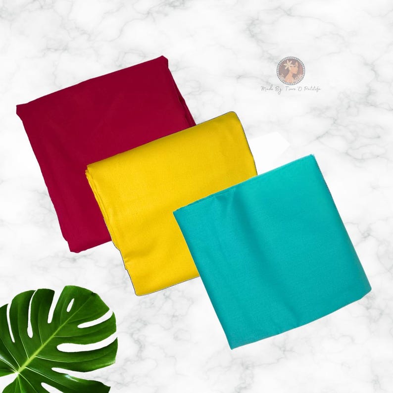 May include: Three folded pieces of fabric in solid colors: deep burgundy, bright yellow, and vibrant turquoise. Each piece is rectangular and smooth in texture. A small circular logo with text is visible in the upper right corner of the image.