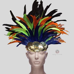Puede incluir: Un tocado de plumas de colores con plumas negras, verdes, azules y naranjas. El tocado está adornado con una banda de metal dorado con detalles decorativos.