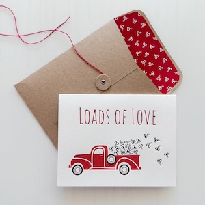 May include: A red truck with a bed full of white hearts, a brown envelope with a red heart pattern, and a card that says "Loads of Love".