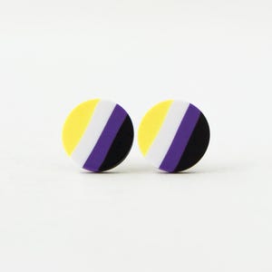 May include: Two round earrings with the non-binary pride flag design. Each earring features a yellow stripe, a white stripe, a purple stripe, and a black stripe. The earrings are set against a white background.