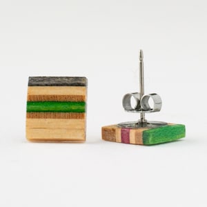 Può includere: Un paio di orecchini quadrati in legno con una striscia verde e un perno in acciaio inossidabile. Gli orecchini sono realizzati in legno di skateboard riciclato.