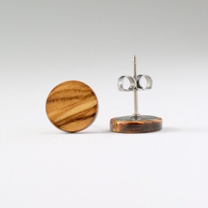 May include: A pair of round wooden earrings with a natural wood grain pattern. The earrings are made of olive wood and have stainless steel posts.
