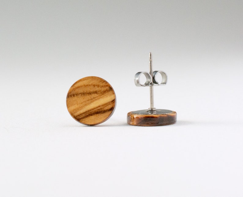 May include: A pair of round wooden earrings with a natural wood grain pattern. The earrings are made of olive wood and have stainless steel posts.