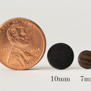 May include: Two round wooden earrings, one black and one brown, next to a US penny for size comparison. The black earring is 10mm in diameter and the brown earring is 7mm in diameter.