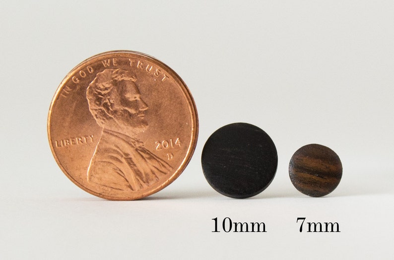 May include: Two round wooden earrings, one black and one brown, next to a US penny for size comparison. The black earring is 10mm in diameter and the brown earring is 7mm in diameter.