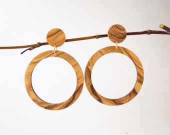 Puede incluir: Un par de pendientes de aro de madera con un acabado de veta de madera natural. Los pendientes están hechos de madera de olivo y tienen un gancho de metal dorado.