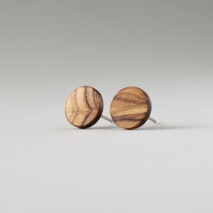 May include: A pair of round wooden earrings with a natural wood grain pattern. The earrings are a light brown color and have silver posts.