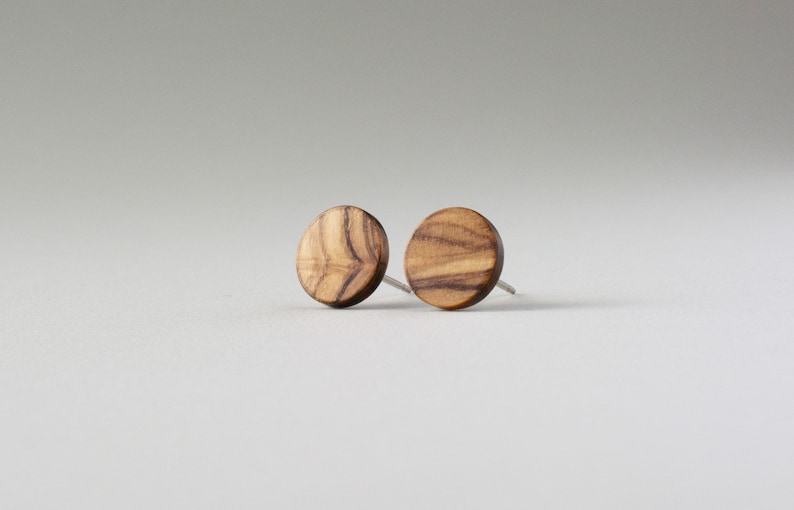 May include: A pair of round wooden earrings with a natural wood grain pattern. The earrings are a light brown color and have silver posts.