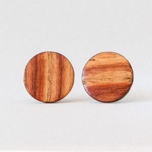 May include: A pair of round wooden earrings with a reddish-brown wood grain pattern.