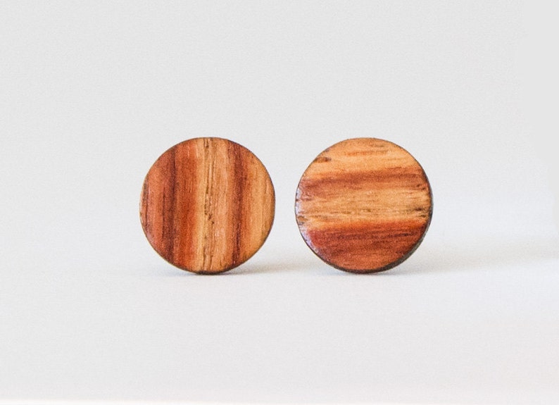 May include: A pair of round wooden earrings with a reddish-brown wood grain pattern.