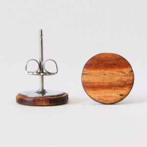 May include: A pair of round wooden earrings with a natural wood grain pattern. The earrings are made of dark brown wood and have a silver post and butterfly back.