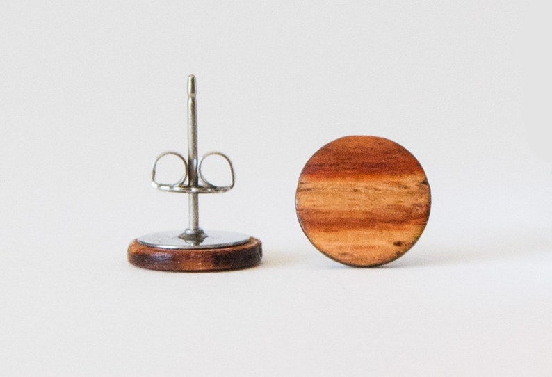 May include: A pair of round wooden earrings with a natural wood grain pattern. The earrings are made of dark brown wood and have a silver post and butterfly back.