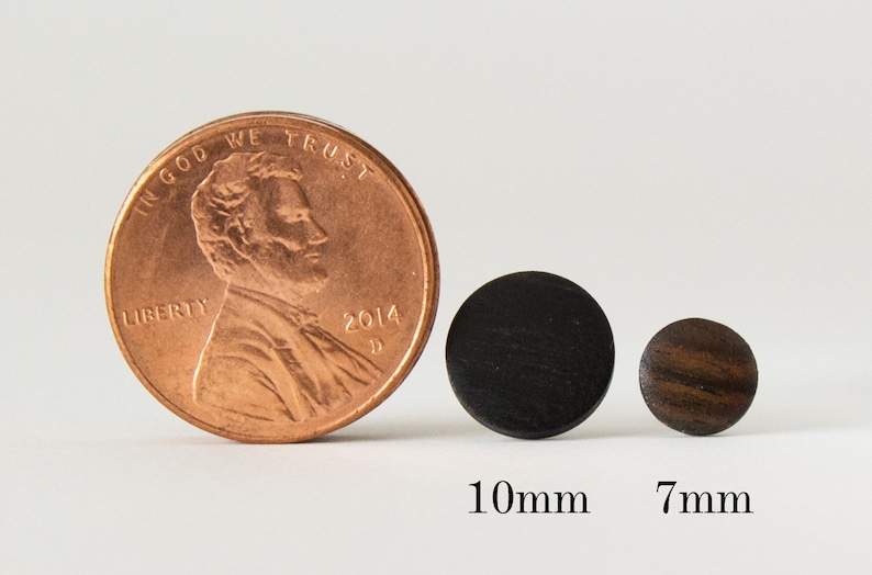 May include: Two round wooden earrings, one black and one brown, shown next to a US penny for size comparison. The black earring is 10mm in diameter and the brown earring is 7mm in diameter.