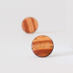 May include: Two round wooden earrings with a striped pattern in shades of brown and red.