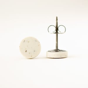 May include: A pair of white stud earrings with a speckled texture. The earrings have silver posts and butterfly backs.