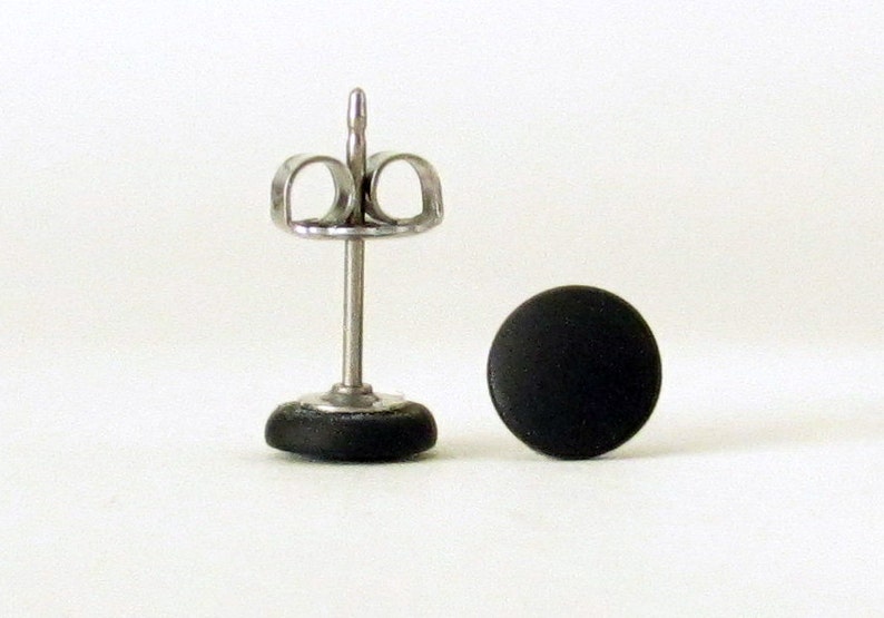 Op de afbeelding: Een paar zwarte oorbel studs met een zilveren pin en vlinder achterkant.