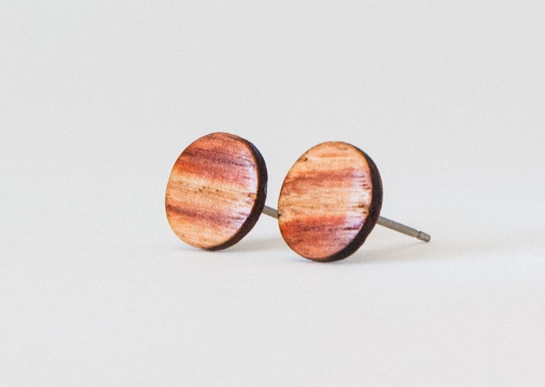 May include: A pair of round wooden earrings with a reddish-brown wood grain pattern. The earrings have silver posts.