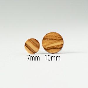 May include: Two round wooden earrings, one is 7mm in diameter and the other is 10mm in diameter. The earrings are made of light brown wood with dark brown streaks.