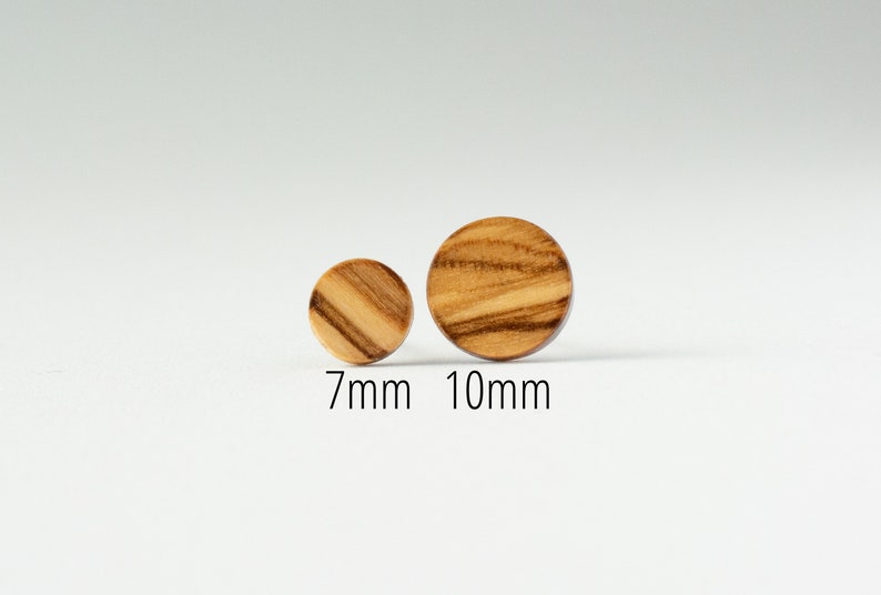 May include: Two round wooden earrings, one is 7mm in diameter and the other is 10mm in diameter. The earrings are made of light brown wood with dark brown streaks.