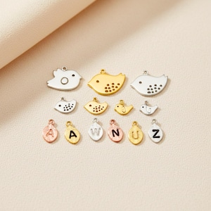 May include: A collection of small bird-shaped charms and letter charms in various metallic finishes. The bird charms are in gold, silver, and white, with dot details. The letter charms include the letters A, W, N, U, and Z.