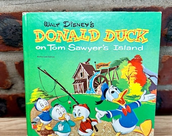 May include: A vintage Whitman Publishing Company book titled "Walt Disney's Donald Duck on Tom Sawyer's Island." The cover features Donald Duck and three nephews in a green field with a gristmill in the background. The book is an authorized edition.
