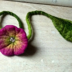 Könnte beinhalten: Eine rosa und grüne Filzblume mit einem silbernen Perlenkern. Die Blume ist an einem grünen Filzstiel befestigt.