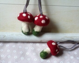 May include: Three felt mushroom ornaments with red caps and white dots, and green stems. The ornaments are hanging from black and white checkered ribbon.