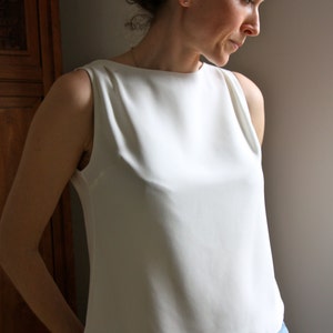 May include: A white sleeveless top with a scoop neck and a slightly flared hem. The top is worn with blue jeans.