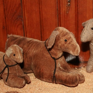 May include: Four plush toy lambs in various shades of brown and gray. The lambs are standing and lying down on a wooden surface.